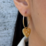 Gold heart-shaped earring worn by a person with a blurred background
