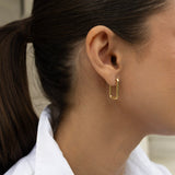 Close-up of a person wearing gold rectangle earring.