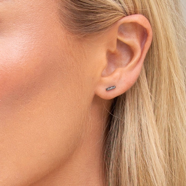 A close-up image of a woman's ear wearing a silver bar stud earring with pave diamonds.