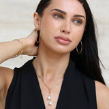 Woman wearing a black top and pearl necklace against a neutral background with Large Oval Gold Hoops
