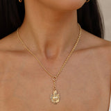 Gold necklace with a leaf pendant worn by a person against a neutral background