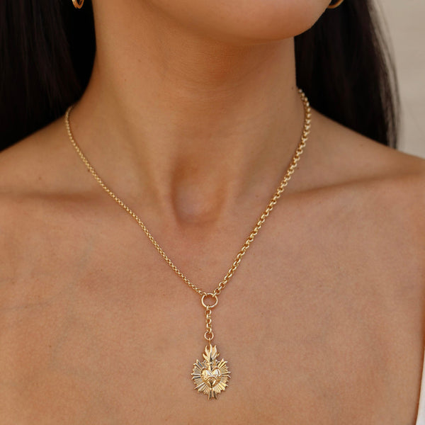 Gold necklace with a leaf pendant worn by a person against a neutral background
