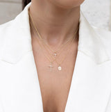 Woman wearing a trio of 14kt gold and diamond crosses in a  white blazer.